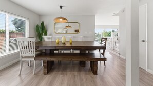 Un coin repas avec une table en bois, des chaises blanches, une suspension et un grand miroir au mur.