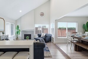 A spacious living area with a fireplace, a dining table set for six, and a large window with blinds.