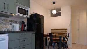 Ett kompakt kök med mikrovågsugn, kylskåp och en matplats med ett träbord och stolar.