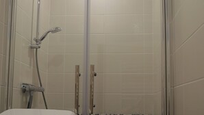 En dusch med en glasdörr, ett vitt badkar och väggar beklädda med svarta kakelplattor.