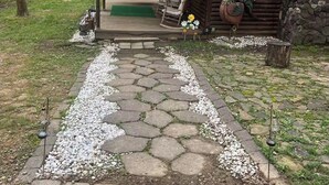 A rustic cabin with a stone pathway leading to a porch, a swing, and a rooster decoration.