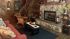 A cozy living room with a stone fireplace, a red sofa, a wicker chair, and a wooden staircase.