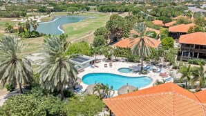 Ett semesterparadis med en swimmingpool, palmer och en golfbana i bakgrunden.