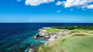 En golfbana vid kusten med klart vatten, klippformationer och utsikt över havet.
