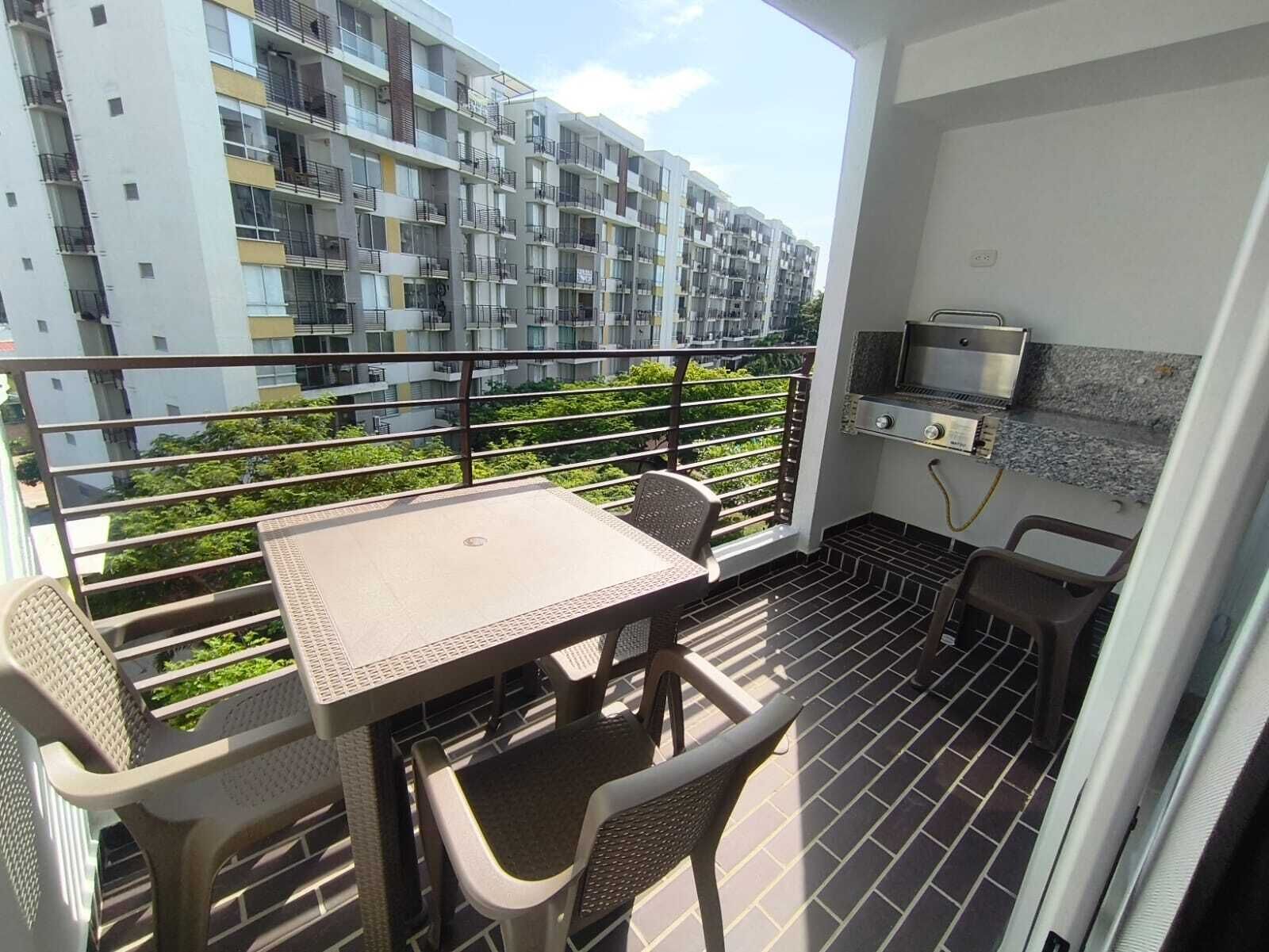 A balcony with a table and chairs, a grill, and a view of a multi-story building.