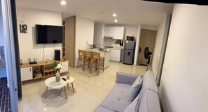 A modern kitchen with a TV, dining area with chairs, a sofa, and a small table with a vase. - Apartamento Familiar en Peñazul Ricaurte Vista a Piscinas Colombia (Ricaurte)