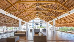 Eine Lounge im Freien mit einem Reetdach, Fliesenböden und Blick auf die umliegenden Gebäude.