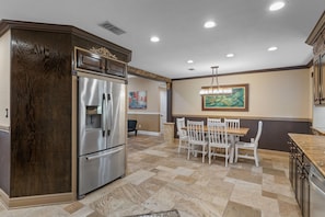 A kitchen with a stainless steel refrigerator, a dining table with chairs, and a painting on the wall.