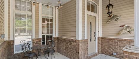 A covered porch with a brick wall, a table with chairs, and decorative wall art.
