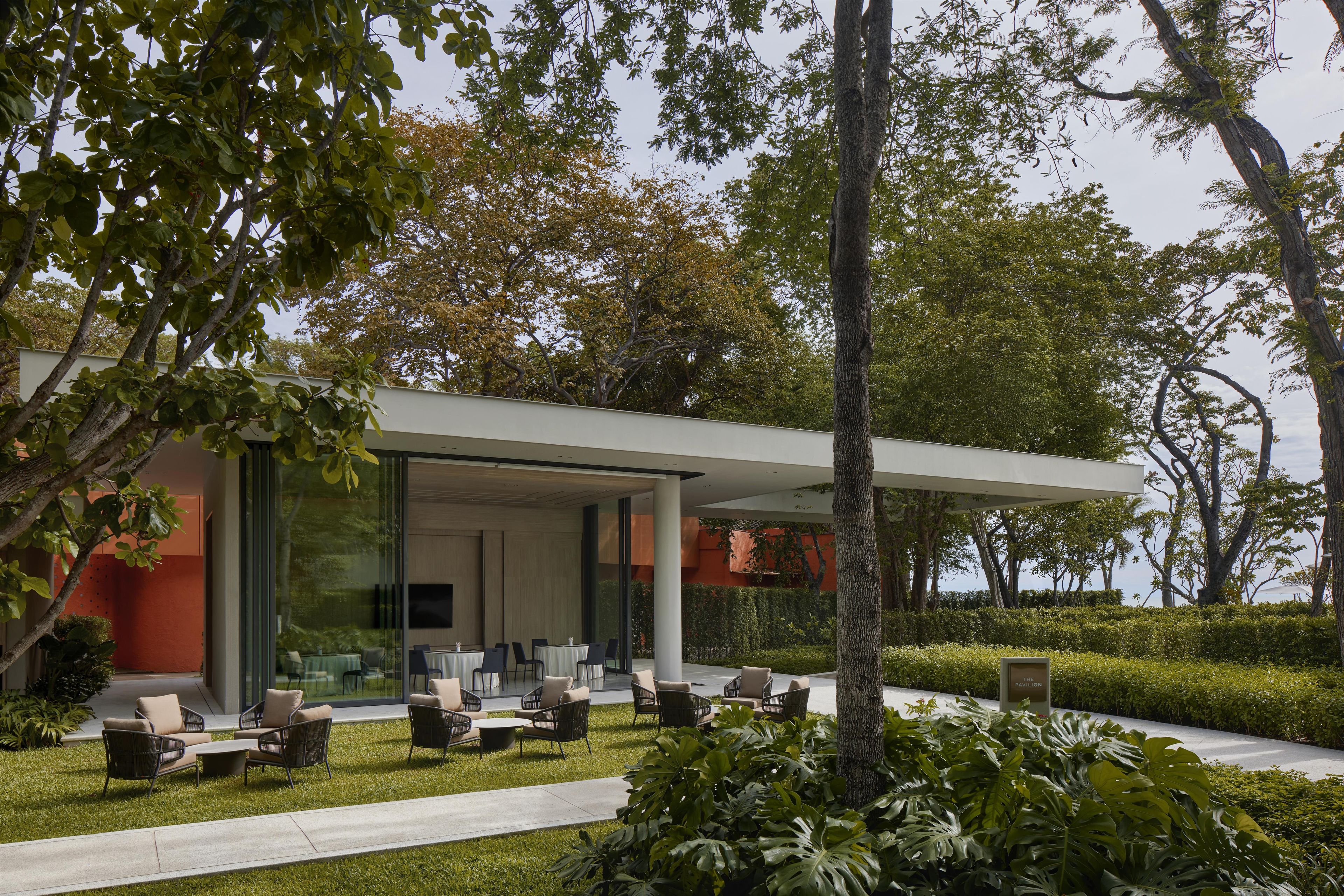 Een modern buitenzitgedeelte met tafels en stoelen, omgeven door weelderig groen en bomen.