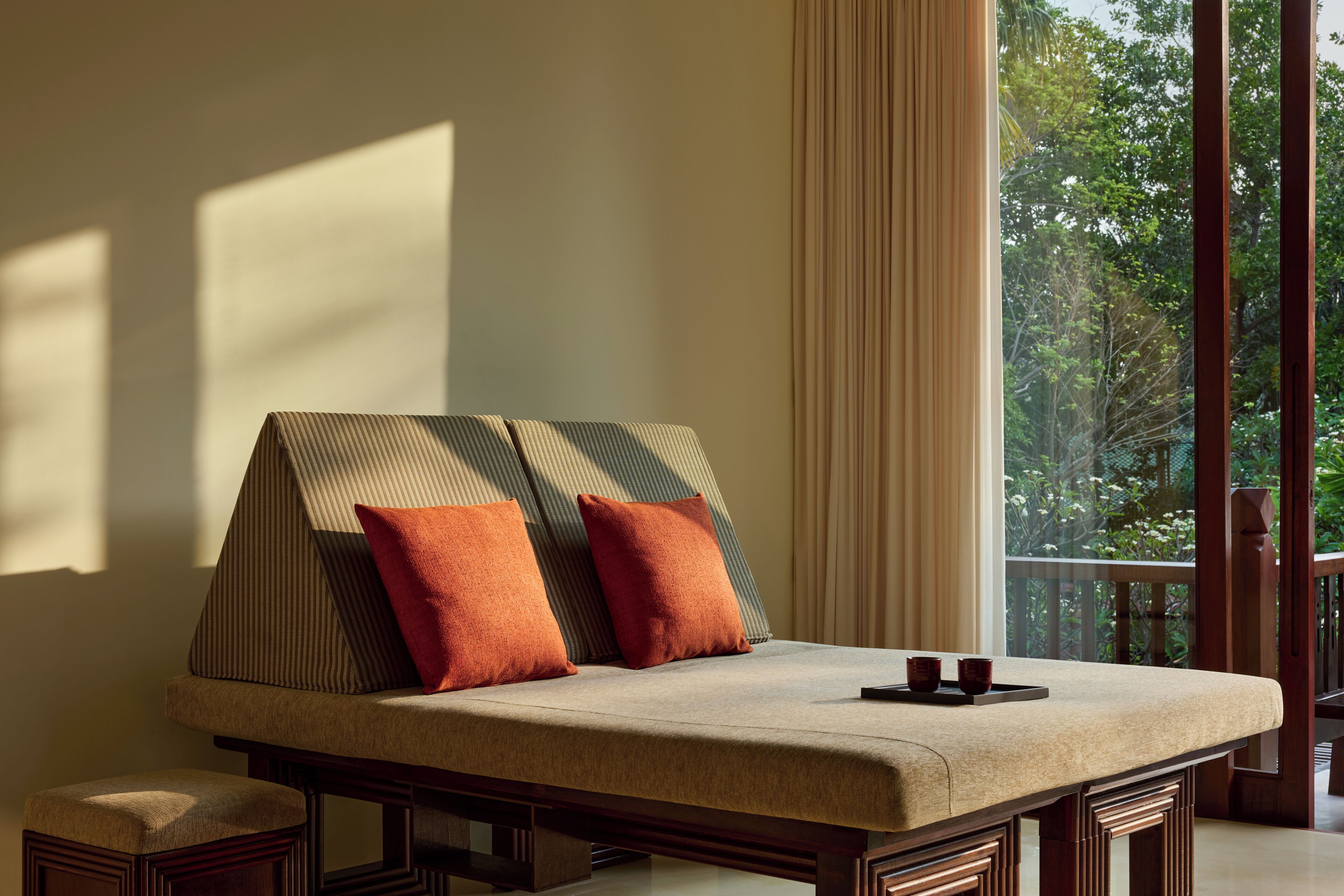 A room with a sofa bed, two pillows, a tray, and a view of greenery through large windows.