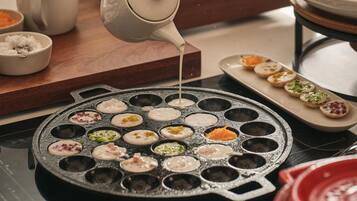 Une personne verse un liquide sur une surface de cuisson chauffée, sur laquelle se trouvent plusieurs moules ronds.