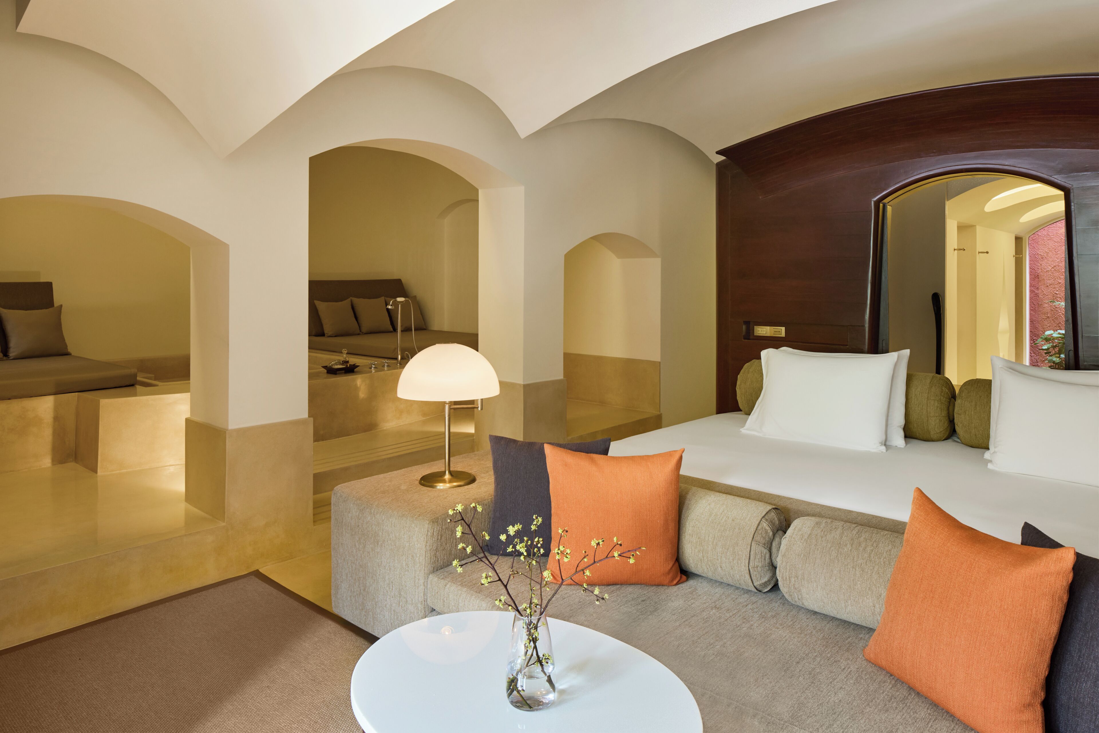 Una habitación de hotel moderna con un sofá, una mesa de centro con un jarrón y un espejo grande.