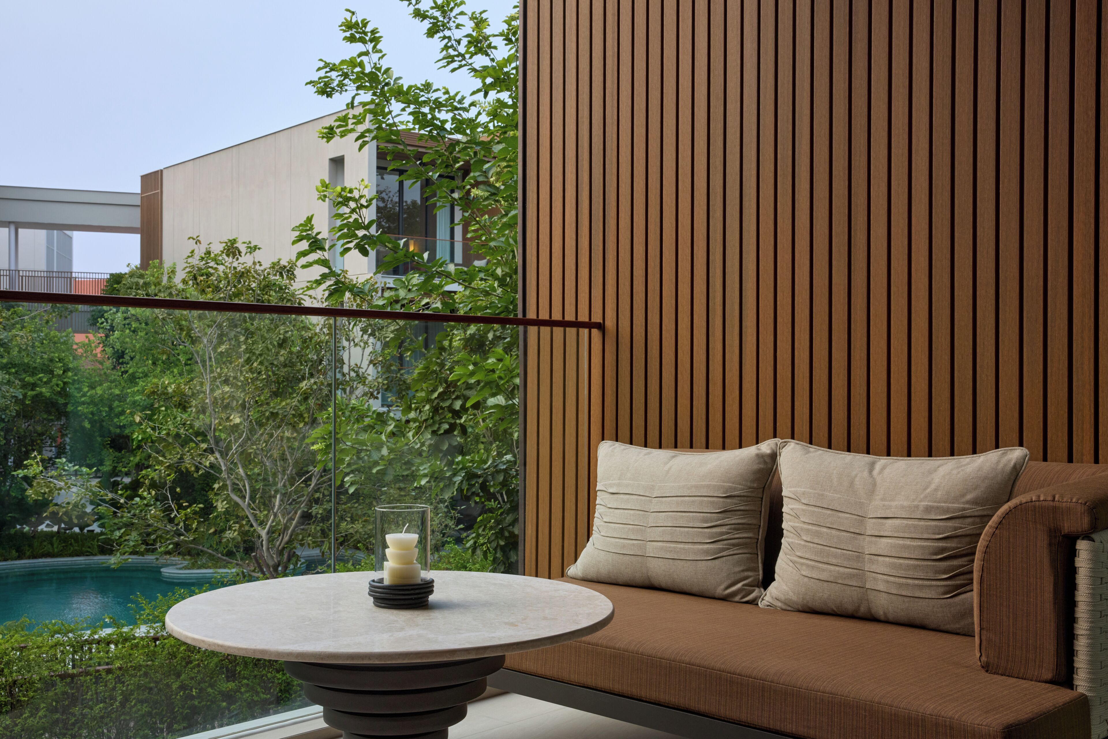 A modern interior with a round table, a sofa with cushions, and a view of greenery and a building.