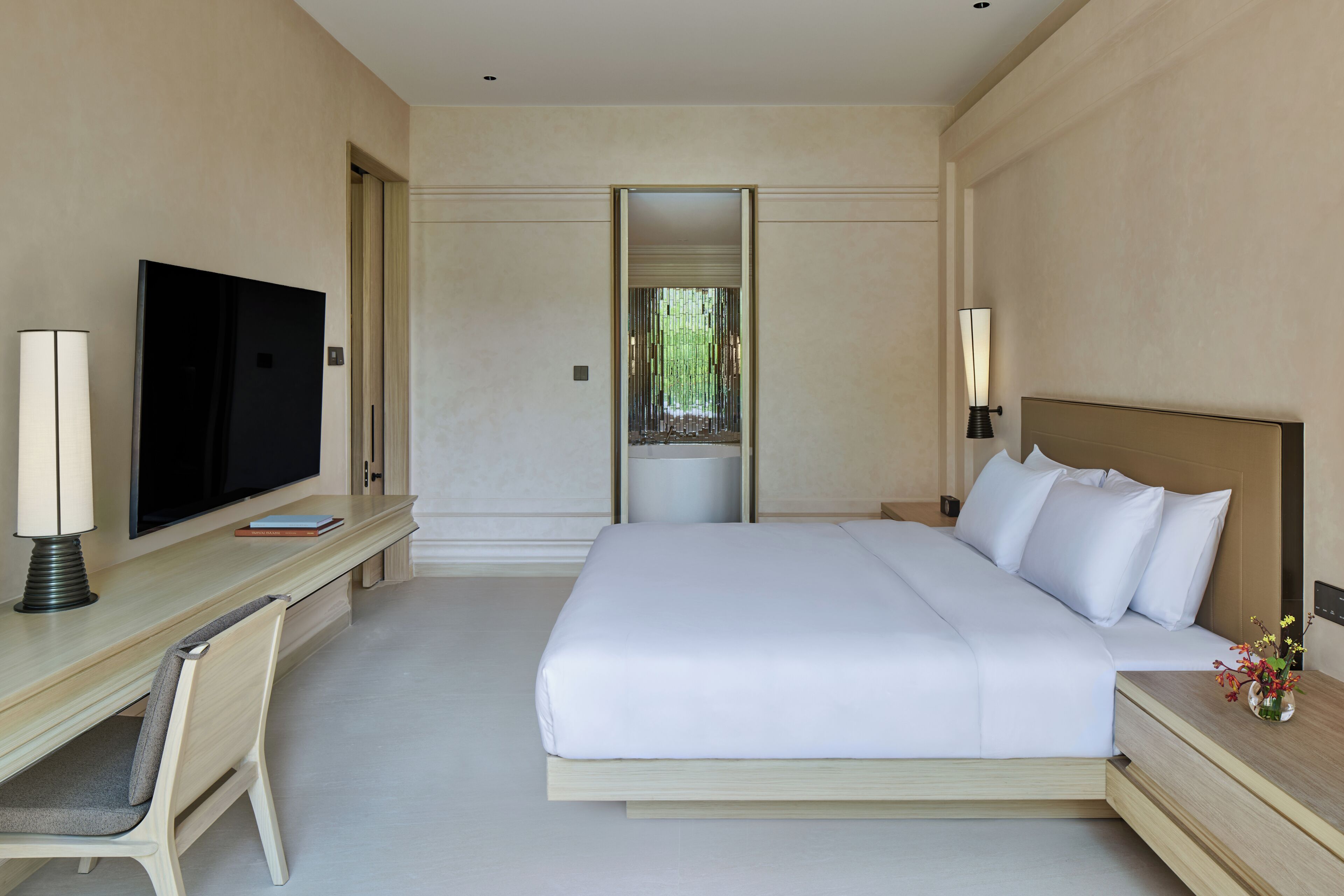 Een hotelkamer met een bed, een bureau met een televisie, een stoel, een nachtkastje met een lamp en een raam met uitzicht.
