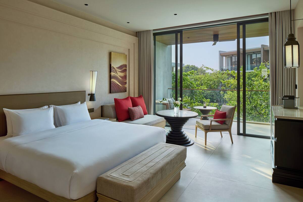 Ein modernes Hotelzimmer mit einem großen Bett, einem kleinen Tisch, einem Sessel und einem Balkon mit Blick.