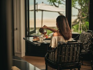 Une personne est assise à une table, et de là, elle a une vue sur la plage grâce à de grandes fenêtres.