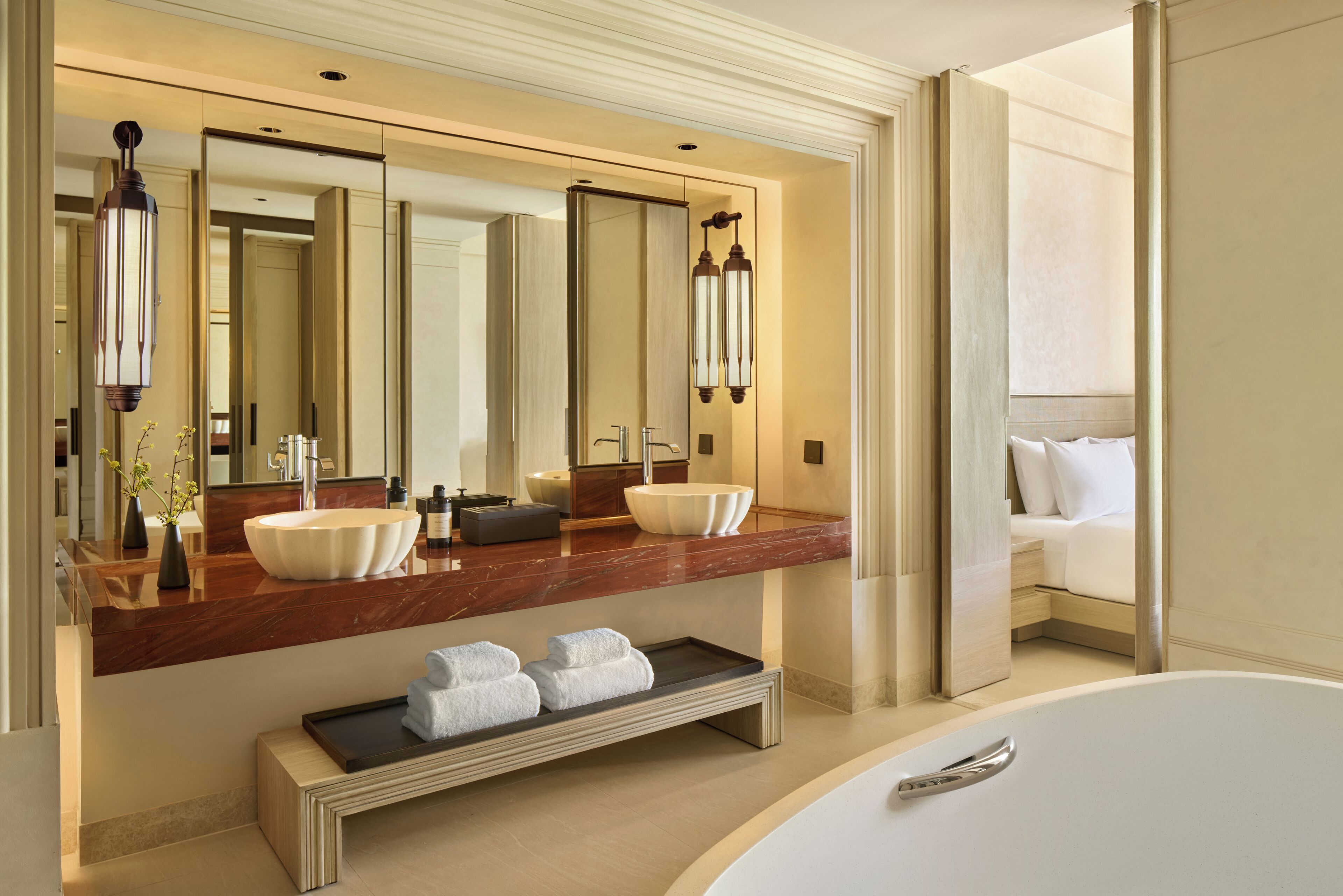 Une salle de bain moderne avec un grand miroir, deux lavabos, une baignoire et un meuble-lavabo sur lequel est posé un plateau contenant des serviettes.