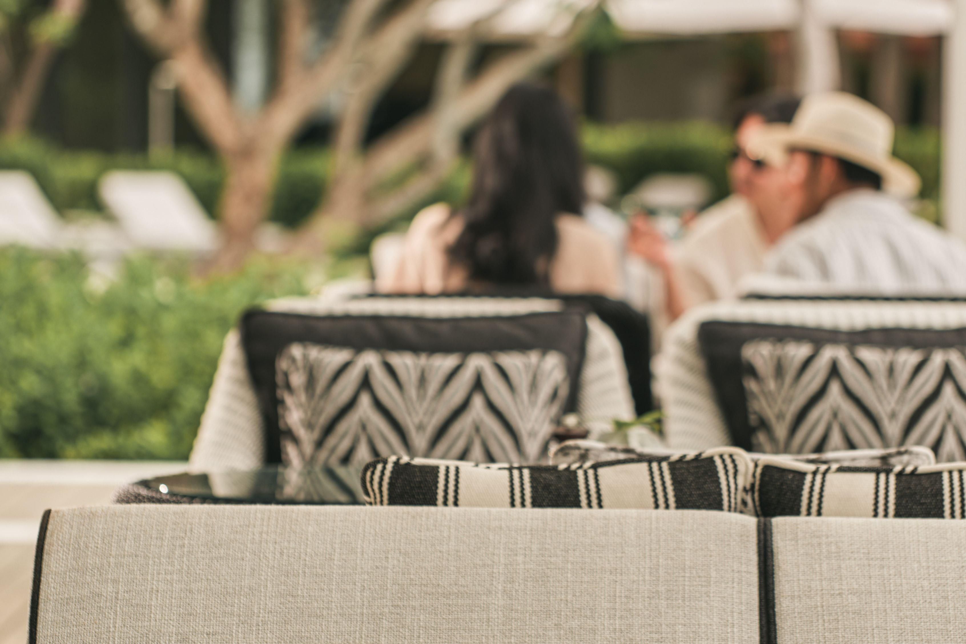 A row of outdoor seating with patterned cushions, a clear sky, and a tree in the background.