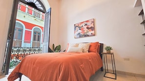 A bedroom with a bed, a painting, a potted plant, and a view of a building through an open door. - Spanish Colonial Retreat in Old San Juan (San Juan)