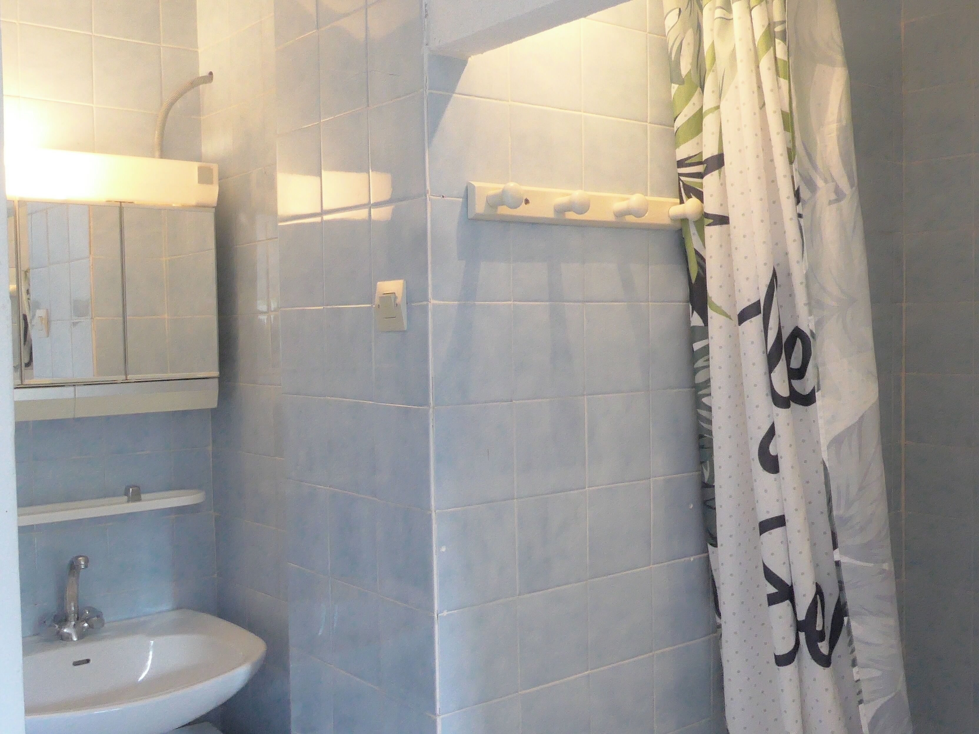 A bathroom with a sink, mirror, shower curtain, and tiled walls.