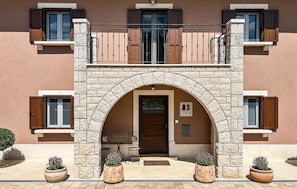 A two-story building with a stone archway entrance, a balcony, and potted plants. - Stunning home in Krsan (Krsan)