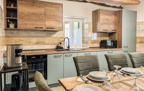 A modern kitchen with wooden cabinets, a built-in oven, a coffee machine, and a dining area with chairs and a table set for two. - Stunning home in Krsan (Krsan)