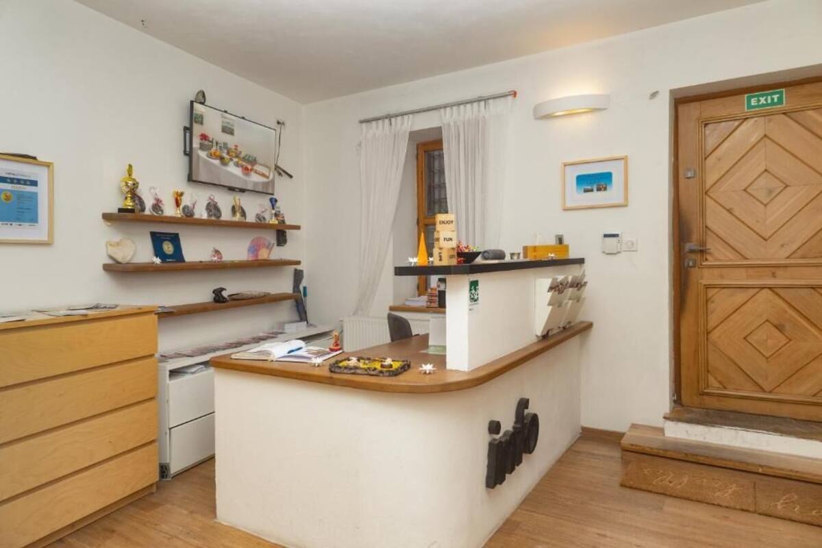 A small, well-lit room with a wooden desk, shelves with awards, a window with curtains, and an exit door.