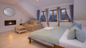 A bedroom with a bed, a sofa, a small table, a fireplace, and large windows with curtains. - Penzion Quest Loket (Loket)