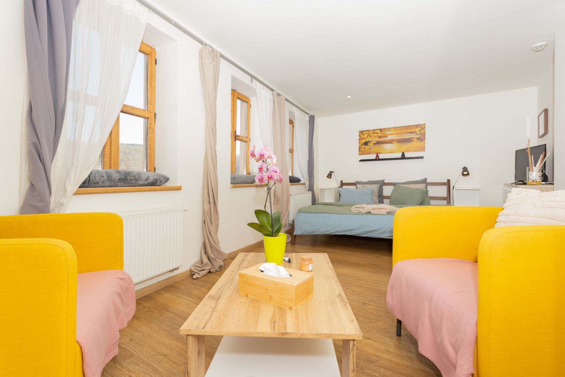 A room with a bed, a yellow sofa, a wooden table with a tissue box, and a window with curtains.