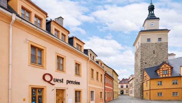 A cobblestone street lined with historic buildings, including a prominent tower with a clock. - Penzion Quest Loket (Loket)