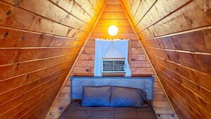 Ett triangulärt rum med träpanel, en säng, ett fönster med gardiner och en synlig lampa.