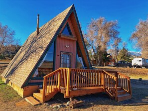 A triangular wooden cabin with a porch, a chimney, and a door. - Riverside A-Frame Cabin Near Salida (Howard)