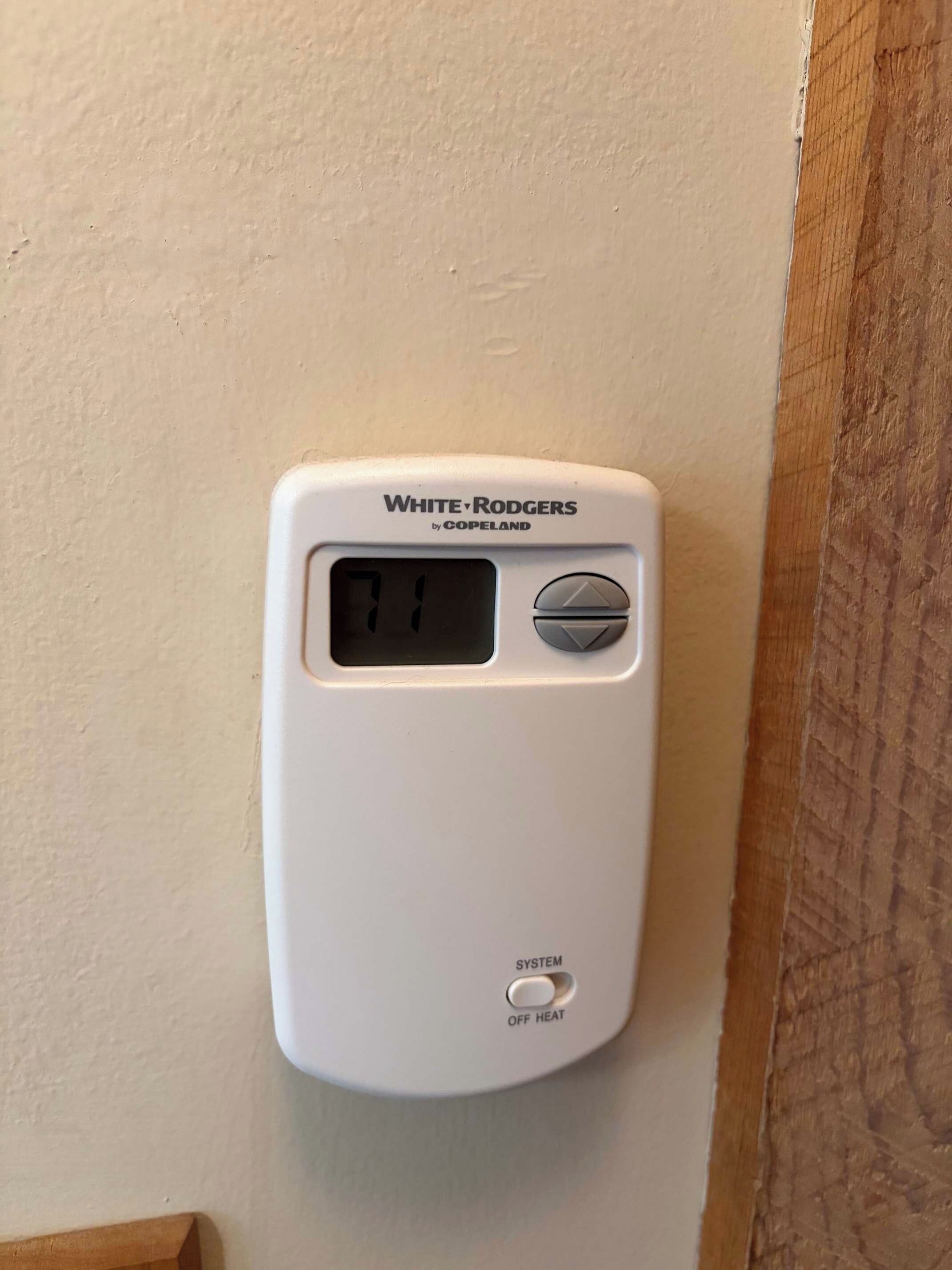 Un termostato blanco con pantalla digital, nombre de marca y un botón de control.