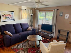 Una sala de estar con un sofá, un televisor sobre un mueble bajo, una mesa redonda y un tapete con motivos florales.
