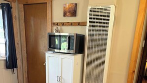 A room with a white cabinet, a microwave on top, a white air conditioner, and a beige sofa with a blue blanket. - Cozy River Cabin with Arkansas River View (Howard)
