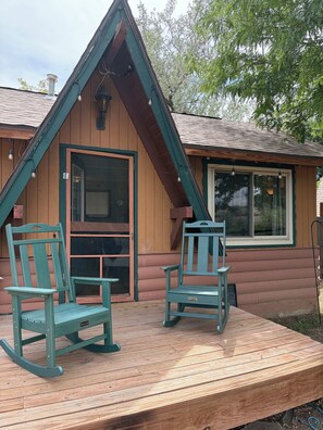 A wooden cabin with a porch, two rocking chairs, and a window.