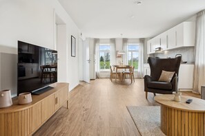 A modern living room with a TV, wooden furniture, a dining area, and a kitchen. - Arrive & feel good in the Altes Land (Mittelnkirchen)
