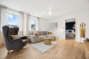 Ein modernes Wohnzimmer mit Sofa, Sessel und rundem Couchtisch.