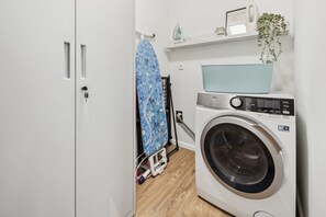 A laundry area with a washing machine, an ironing board, and a shelf with a plant. - Arrive & feel good in the Altes Land (Mittelnkirchen)