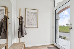 Ein Zimmer mit Kleiderhaken, einem gerahmten Kunstwerk, einer Bank und einer zur Außenseite führenden Tür.