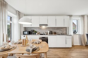 Eine moderne Küche mit weißen Schränken, eine Essecke mit Holzmöbeln und großen Fenstern.