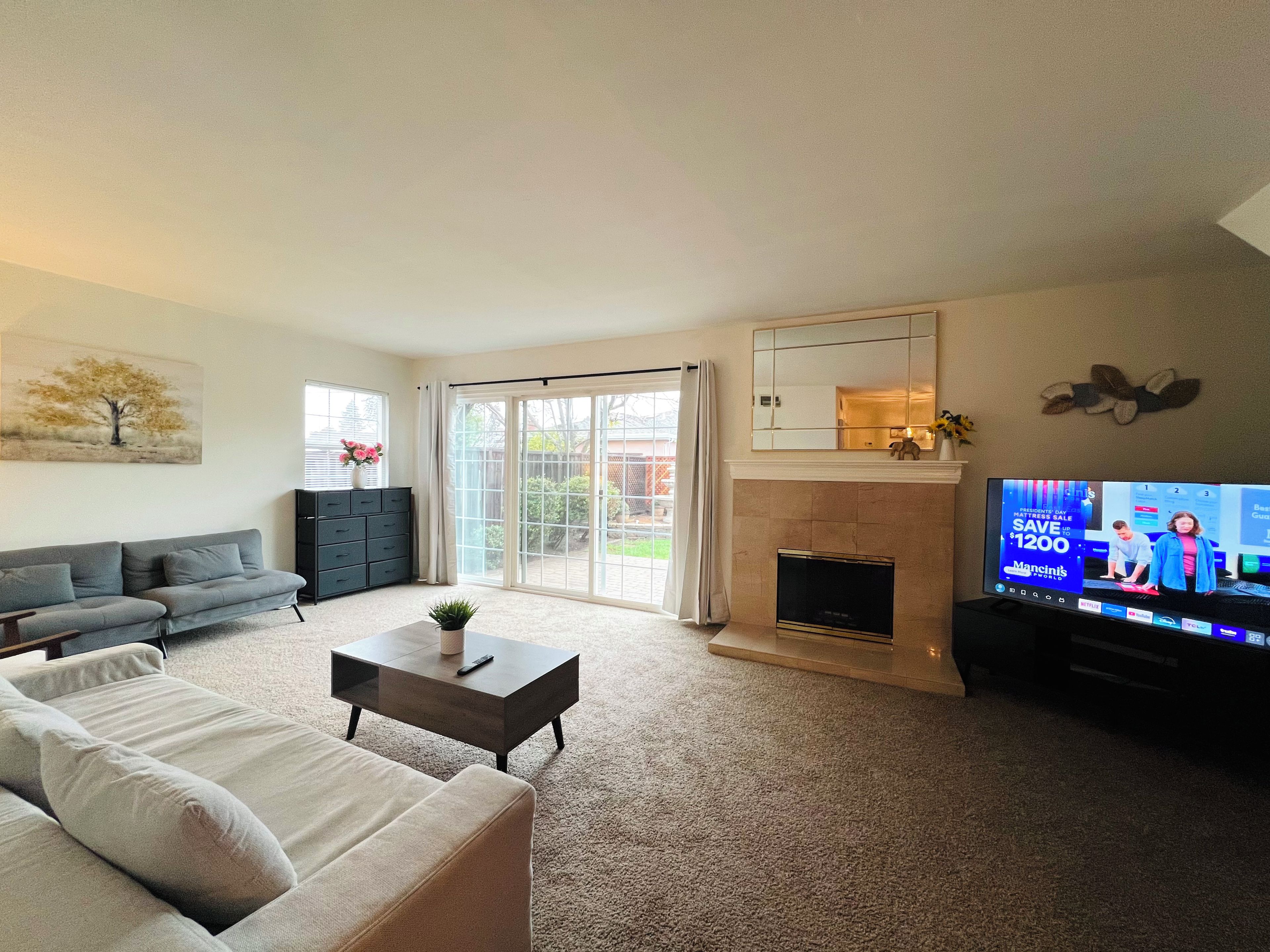 A living room with a sofa, coffee table, fireplace, and a television displaying a show.