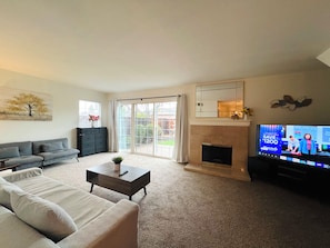 A living room with a sofa, coffee table, fireplace, and a television displaying a show. - Spacious 6-bedroom house in delightful San Jose with AC (San Jose)
