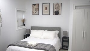 Ein Schlafzimmer mit einem Bett, Nachttischen, einem Kleiderschrank und drei gerahmten Kunstwerken an der Wand.