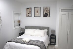 Ein Schlafzimmer mit einem Bett, Nachttischen, einem Kleiderschrank und drei gerahmten Kunstwerken an der Wand.