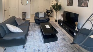 Ein modernes Wohnzimmer mit Sofa, Sessel, Couchtisch, Fernseher und Kunstwerken an der Wand.