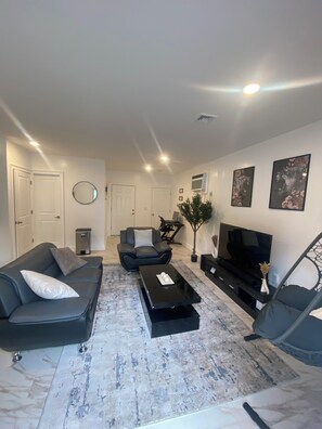Ein modernes Wohnzimmer mit Sofa, Sessel, Couchtisch, Fernseher und Kunstwerken an der Wand.