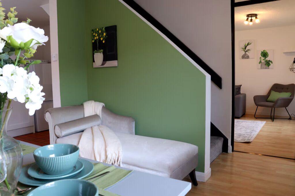 A living room with a sofa, a dining table with plates, a vase with flowers, and a staircase.