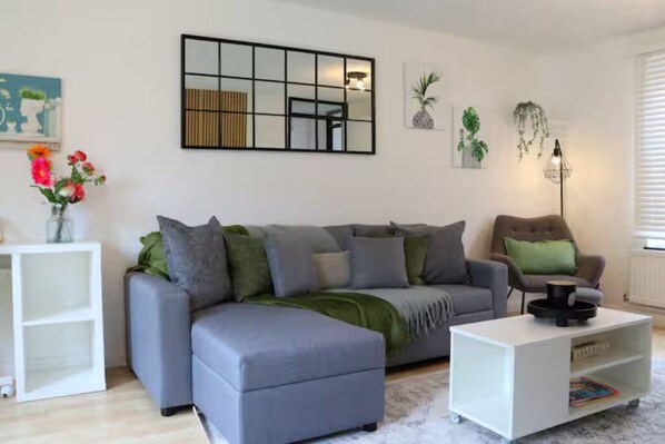 A modern living room with a grey sectional sofa, a white coffee table, and a white side table with a vase of flowers.